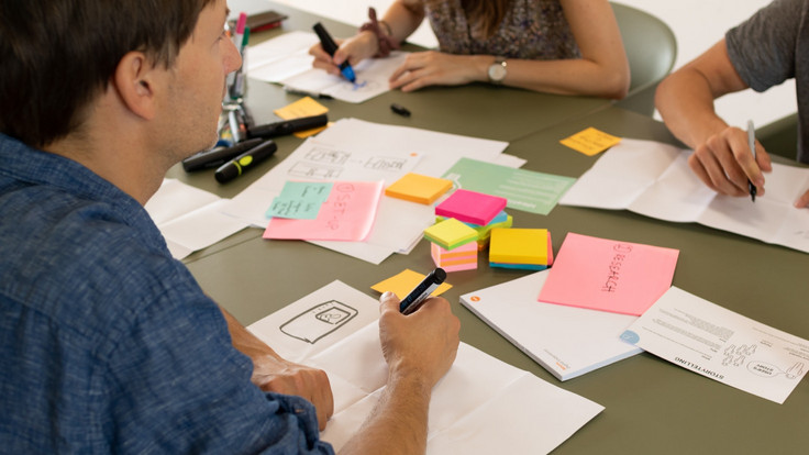 Workshopteilnehmer:innen sitzen mit Stiften und Klebezetteln an einem Tisch